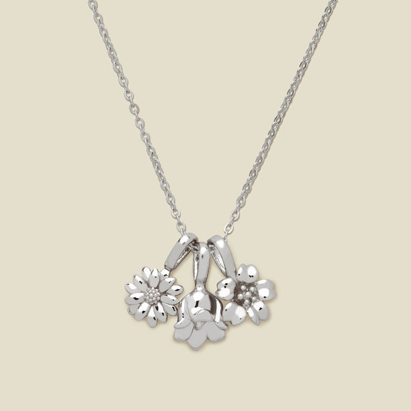 As silver pendant necklace with three small flower charms, shown on a solid light beige background.