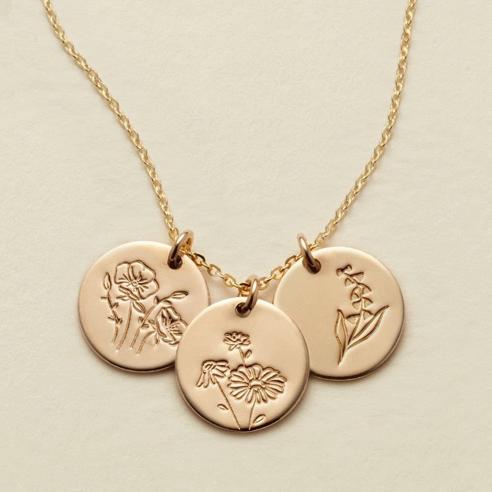 A gold chain necklace with three round engraved disc pendants featuring floral  designs, displayed on a light beige background.