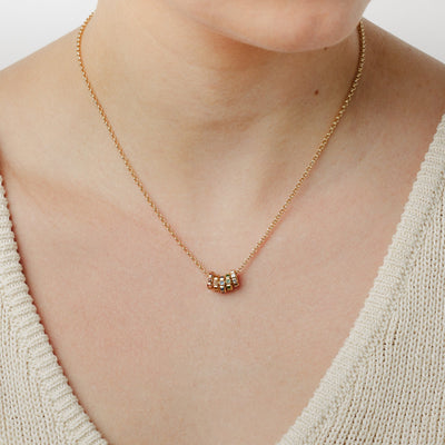 A close-up lifestyle image of a person wearing a gold chain chain necklace with five small ring charms, each with a different color of gemstone, set against a white background.