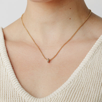 A close-up lifestyle image of a person wearing a gold chain chain necklace with a small ring charm in an eternity style with blue square gemstones, set against a white background.