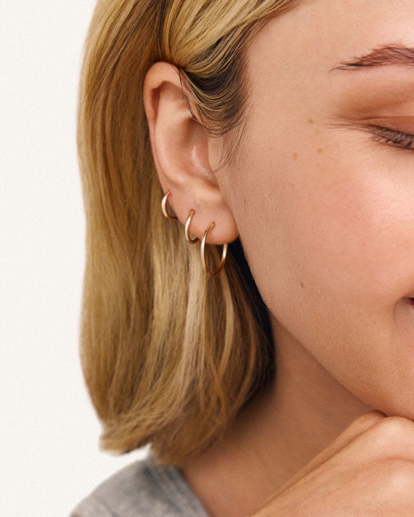 A model wearing three sizes of thin gold hoop earrings in one ear.