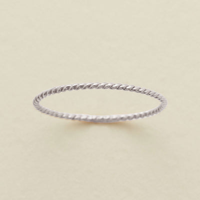 A thin, twisted rope-style ring in a silver metal, photographed on a clean, light beige textured background.