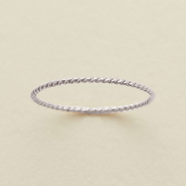 A thin, twisted rope-style ring in a silver metal, photographed on a clean, light beige textured background.