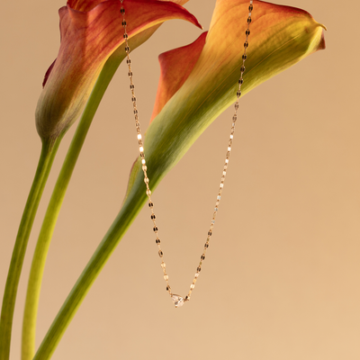 Delicate gold necklace with a clear tear-drop shaped clear stone on a calla lily against a beige background