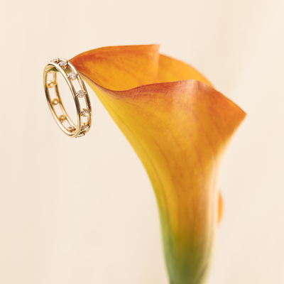 Gold ring with small marquise-cut clear stones on an orange flower against a beige background