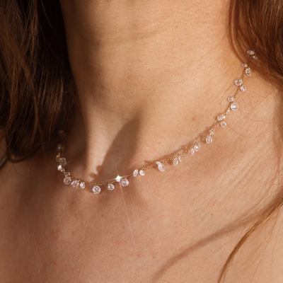 A close up lifestyle shot of a person's neck wearing a gold chain necklace with clusters of round clear crystals dangling down