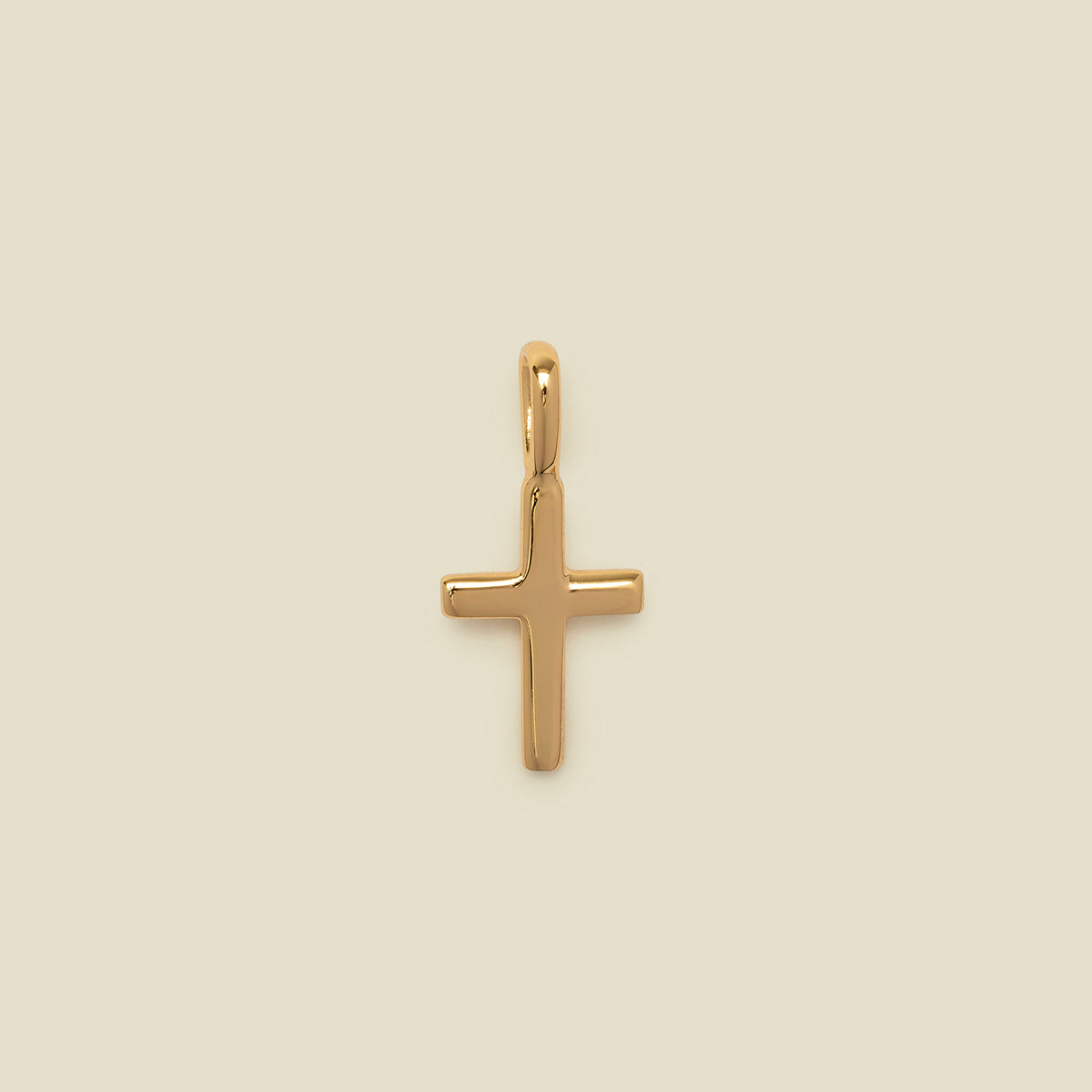 A polished gold cross pendant with a smooth, rounded finish and a top loop, centered on a solid, warm beige background.