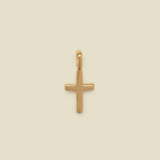A polished gold cross pendant with a smooth, rounded finish and a top loop, centered on a solid, warm beige background.