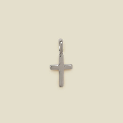 A polished silver cross pendant with a smooth, rounded finish and a top loop, centered on a solid, warm beige background.