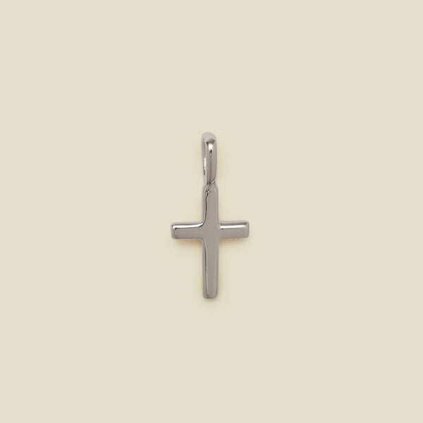 A polished silver cross pendant with a smooth, rounded finish and a top loop, centered on a solid, warm beige background.