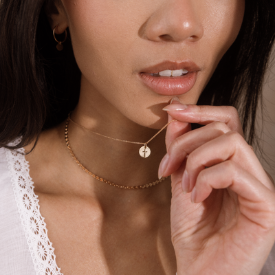 Close-up of a woman wearing delicate gold necklaces, including a fine chain with a small round cross pendant and a textured chain.