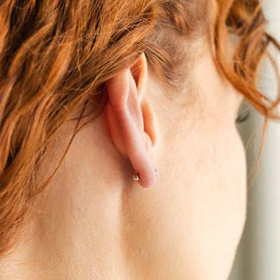 A close-up of the back of a person's ear showing a round ball backing for a stud earring.