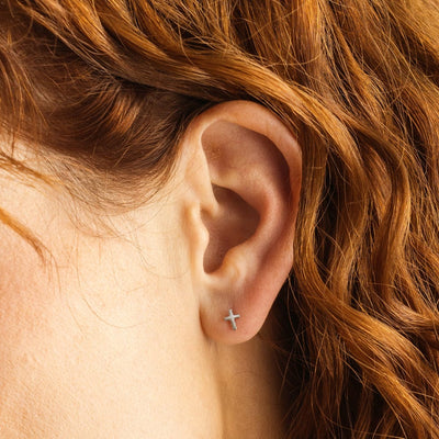 A close-up of a person's ear wearing a silver cross stud earring.
