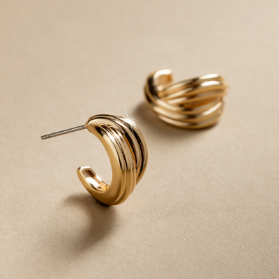 A pair of gold, textured hoop earrings with intertwining strands crossed over, set against a textured beige background.