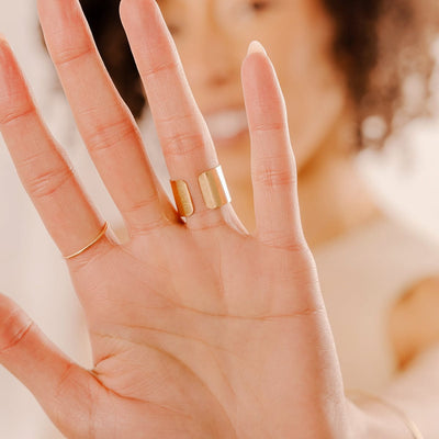 A close-up of a person's palm wearing a thin gold wire ring and a wide polished gold cigar band ring.