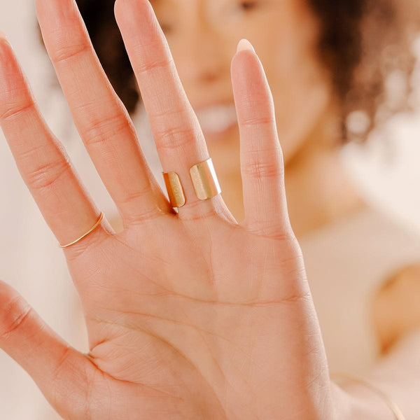 A close-up of a person's palm wearing a thin gold wire ring and a wide polished gold cigar band ring.