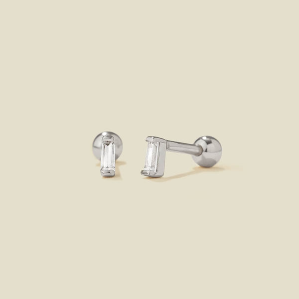 A pair of silver stud earrings with baguette-cut clear gemstones, shown on a solid light beige background.