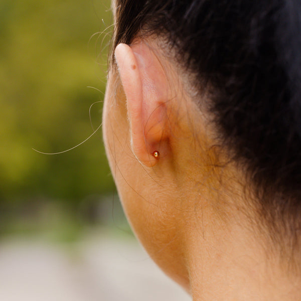 The back of a person's ear, showcasing a round gold earring backing.