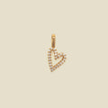 A gold heart-shaped pendant charm paved with small clear stones, shown against a solid beige background.