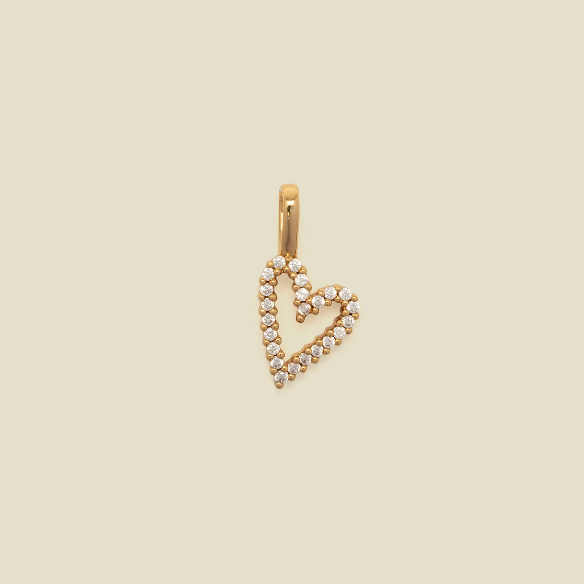A gold heart-shaped pendant charm paved with small clear stones, shown against a solid beige background.