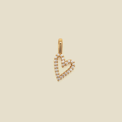 A gold heart-shaped pendant charm paved with small clear stones, shown against a solid beige background.