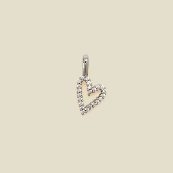 A silver heart-shaped pendant charm paved with small clear stones, shown against a solid beige background.