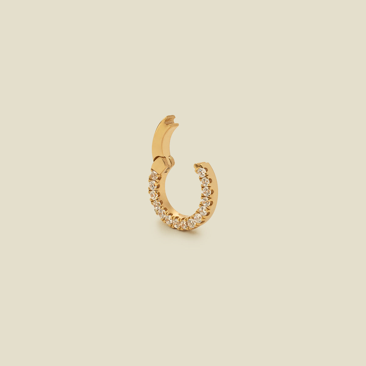 A small gold ring necklace attachment embellished with a row of clear pavé-set stones, shown on a solid beige background.