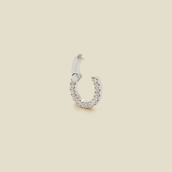 A small silver ring necklace attachment embellished with a row of clear pavé-set stones, shown with the latch open on a solid beige background.