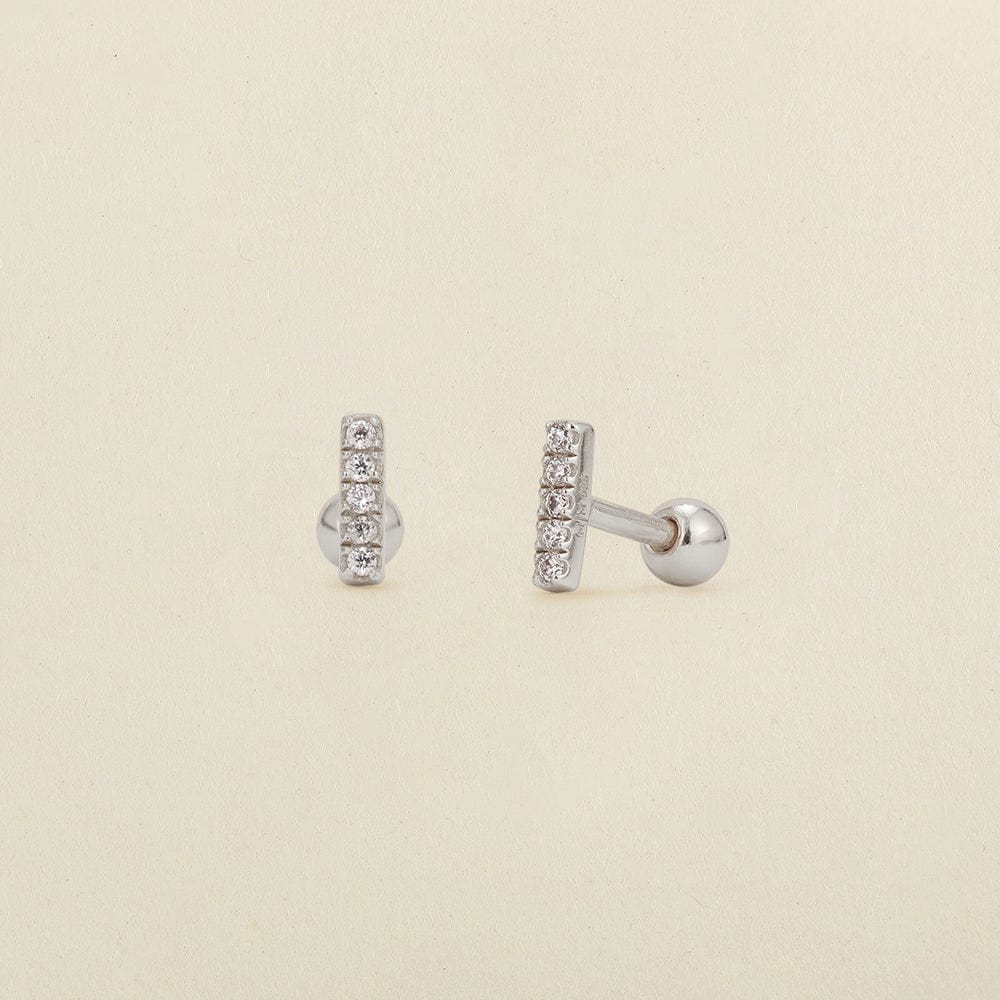 A pair of silver stud earrings with a vertical bar set with clear cubic zirconia stones, shown on a light beige textured background.