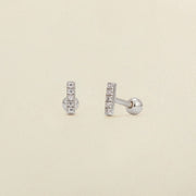 A pair of silver stud earrings with a vertical bar set with clear cubic zirconia stones, shown on a light beige textured background.
