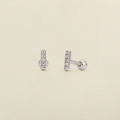 A pair of silver stud earrings with a vertical bar set with clear cubic zirconia stones, shown on a light beige textured background.
