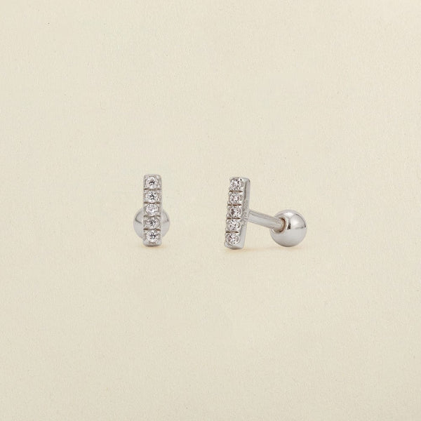 A pair of silver stud earrings with a vertical bar set with clear cubic zirconia stones, shown on a light beige textured background.