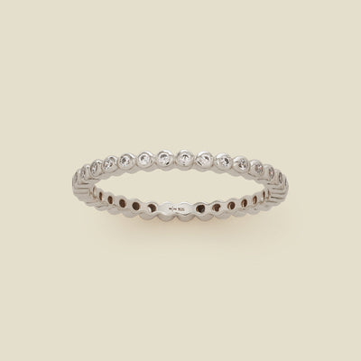 A silver eternity ring featuring a continuous row of bezel-set clear round gemstones on a light beige background.