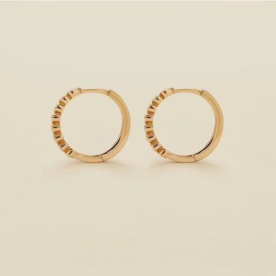 A pair of gold hoop earrings standing upright against a solid beige background.
