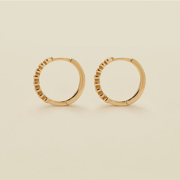 A pair of gold hoop earrings standing upright against a solid beige background.