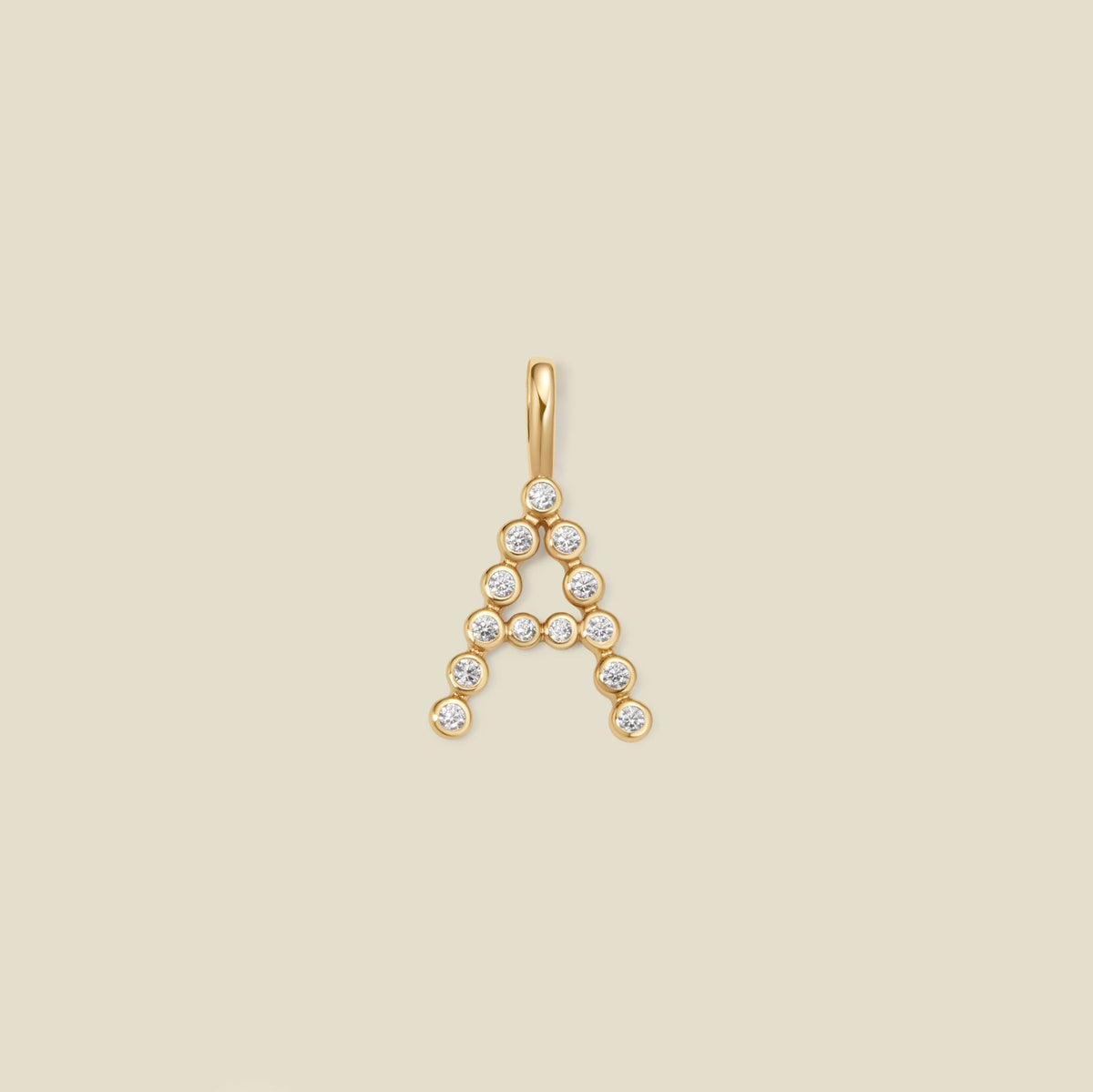 A gold letter 'A' pendant charm embellished with small clear round gemstones, centered on a solid light beige background.