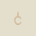 A gold letter 'C' pendant charm embellished with small clear round-cut gemstones, shown on a solid light beige background.