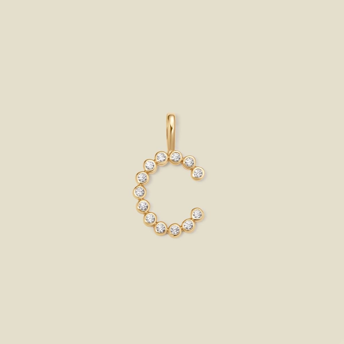 A gold letter 'C' pendant charm embellished with small clear round-cut gemstones, shown on a solid light beige background.