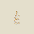 A gold letter 'E' pendant charm embellished with small clear round gemstones, centered on a solid light beige background.