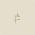 A gold letter 'F' pendant charm embellished with small clear round gemstones, centered on a solid light beige background.