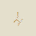 A gold letter 'H' pendant charm embellished with small clear gemstones, set against a solid light beige background.