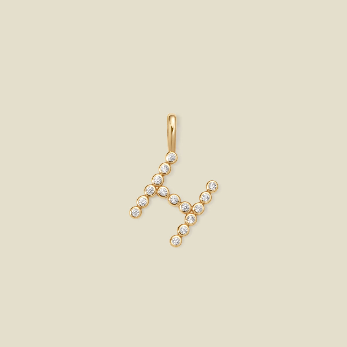 A gold letter 'H' pendant charm embellished with small clear gemstones, set against a solid light beige background.