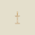 A gold initial pendant charm shaped like the letter 'I', adorned with small clear gemstones, centered on a solid beige background.