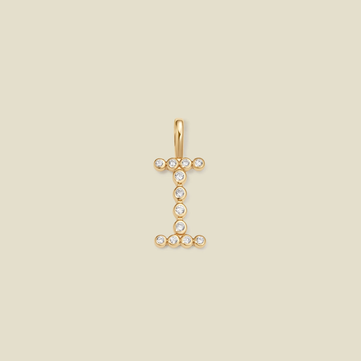 A gold initial pendant charm shaped like the letter 'I', adorned with small clear gemstones, centered on a solid beige background.