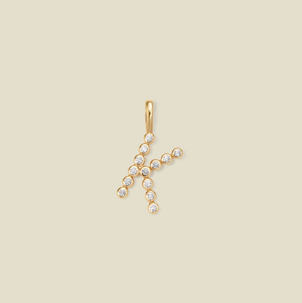 A gold initial pendant shaped like the letter 'K', adorned with small clear gemstones, centered on a solid beige background.