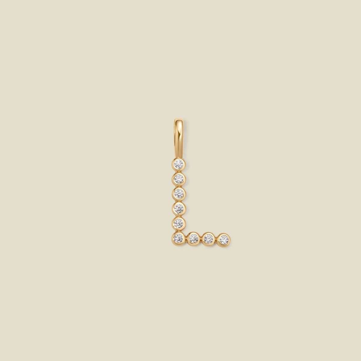A gold initial pendant shaped like the letter 'L', adorned with small clear gemstones, centered on a solid light beige background.