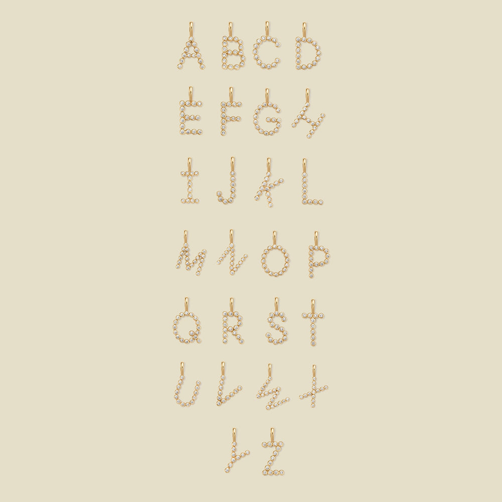 A layout of 26 letter charms, showing uppercase letters A through Z, each formed from small gold-toned circular elements arranged vertically, on a plain warm beige background.
