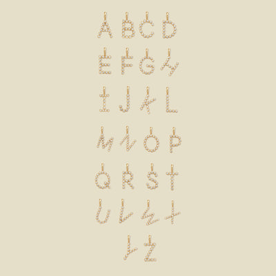 A layout of 26 letter charms, showing uppercase letters A through Z, each formed from small gold-toned circular elements arranged vertically, on a plain warm beige background.