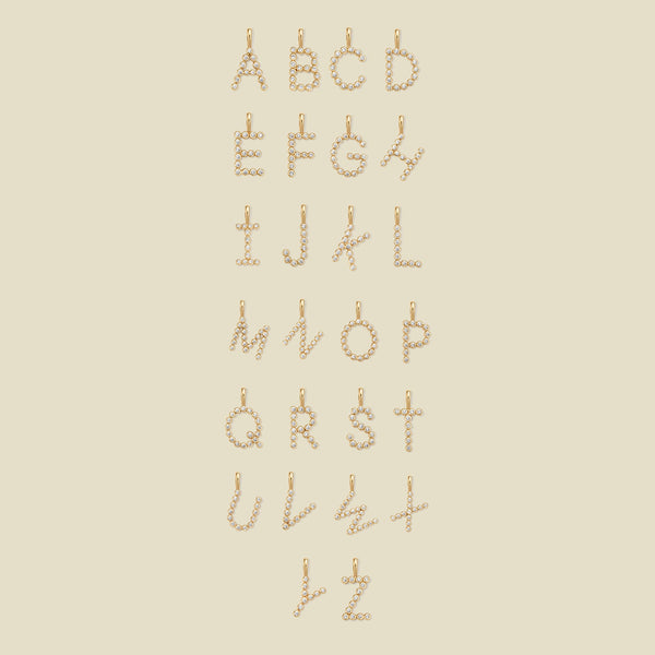 A layout of 26 letter charms, showing uppercase letters A through Z, each formed from small gold-toned circular elements arranged vertically, on a plain warm beige background.