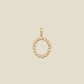 A gold initial 'O' charm featuring small clear round-cut stones, set against a solid light beige background.